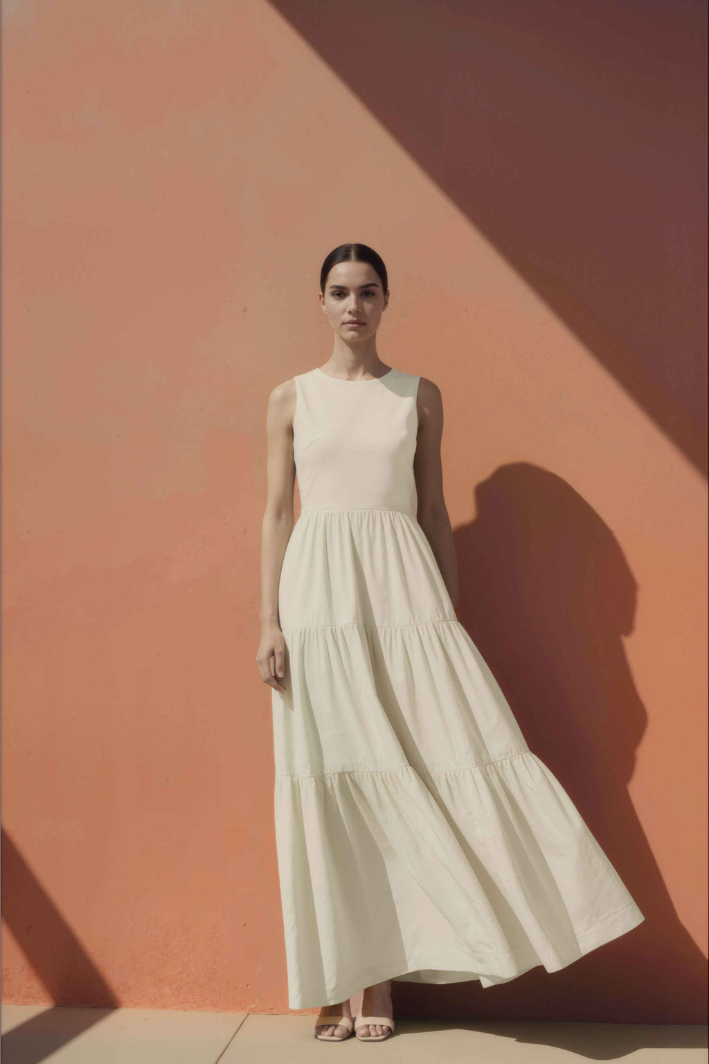Woman in a white cotton maxi dress standing against a pink wall.