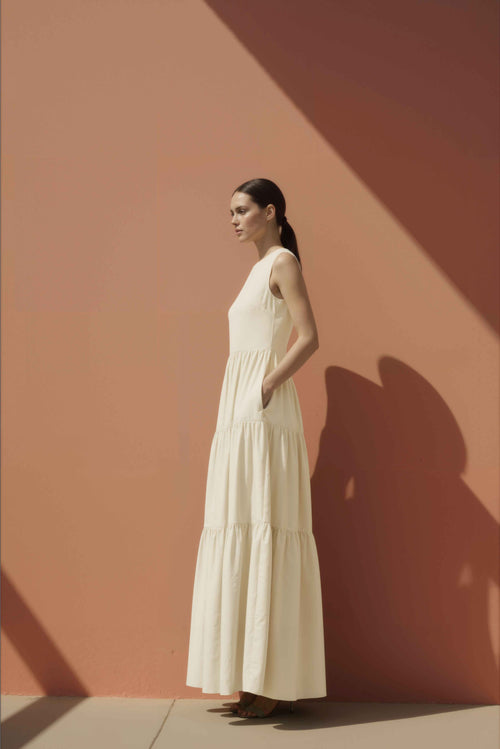 Woman in a white cotton maxi dress standing against a pink wall.