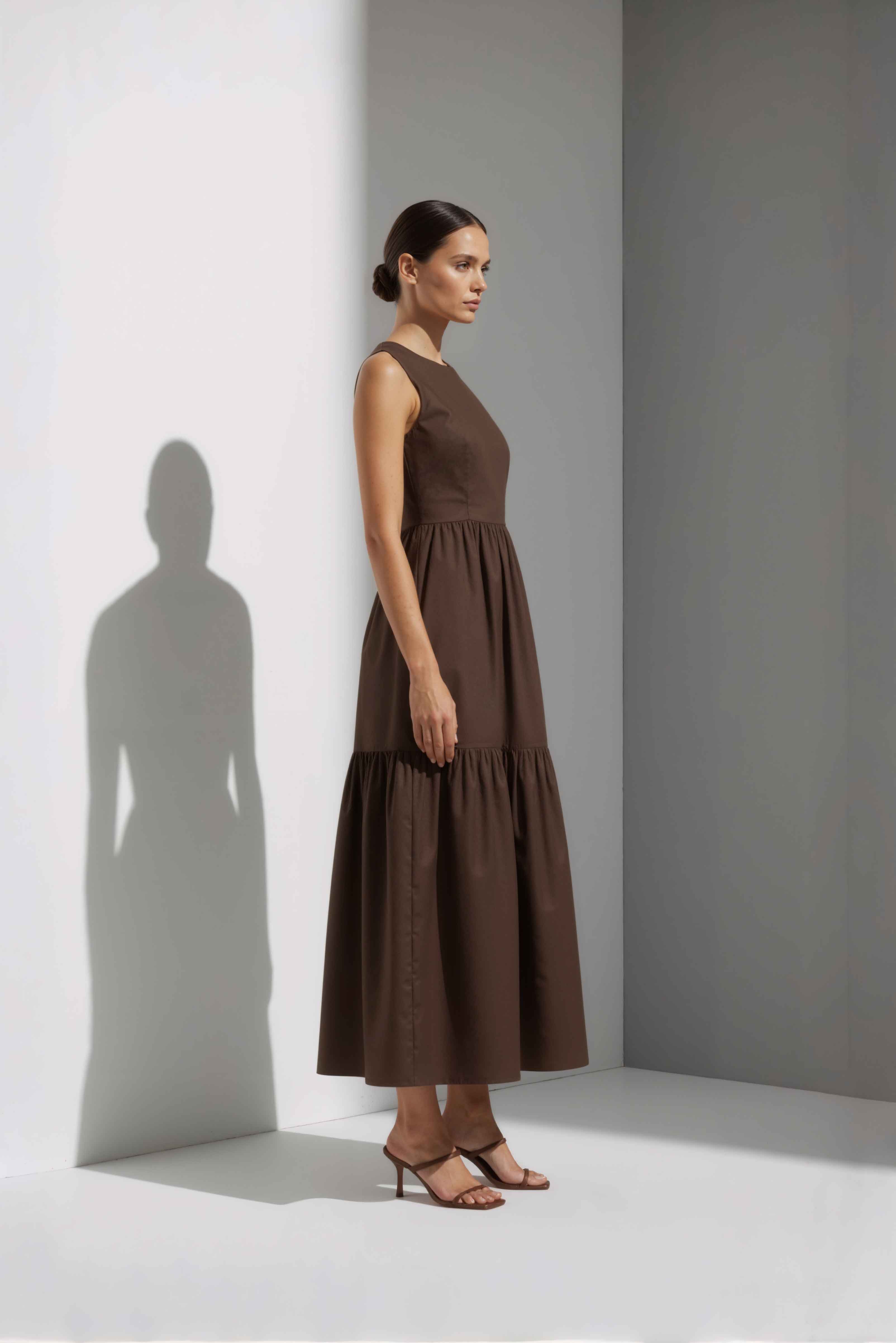 Anasua The Forme Edit Poplin Cotton Midi Dress in Umber Brown, a structured sleeveless cotton midi dress with a tiered skirt, photographed under natural sunlight.