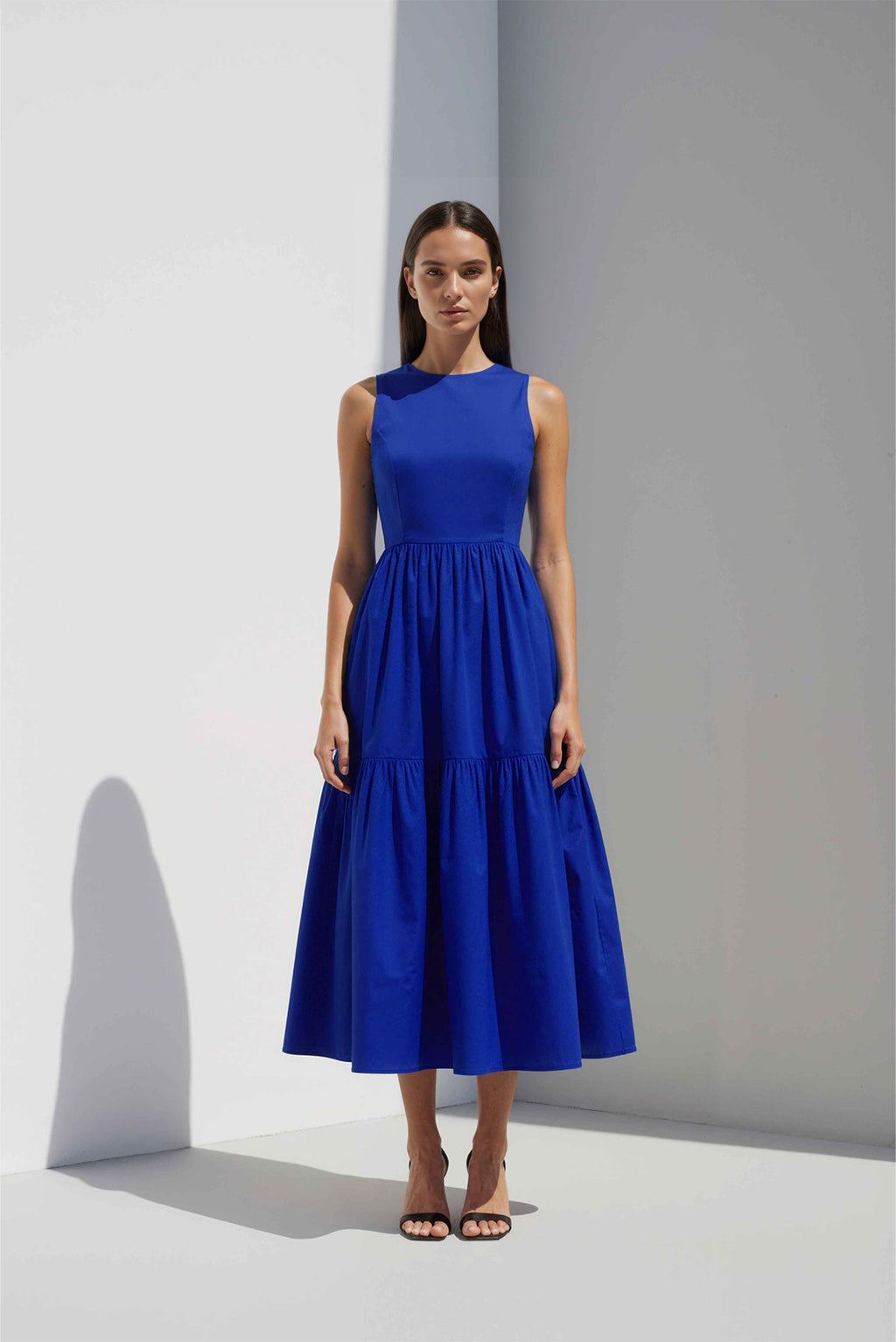 Anasua The Forme Edit Poplin Cotton Midi Dress in Sand Grey, a structured sleeveless cotton midi dress with a tiered skirt, photographed under natural sunlight.