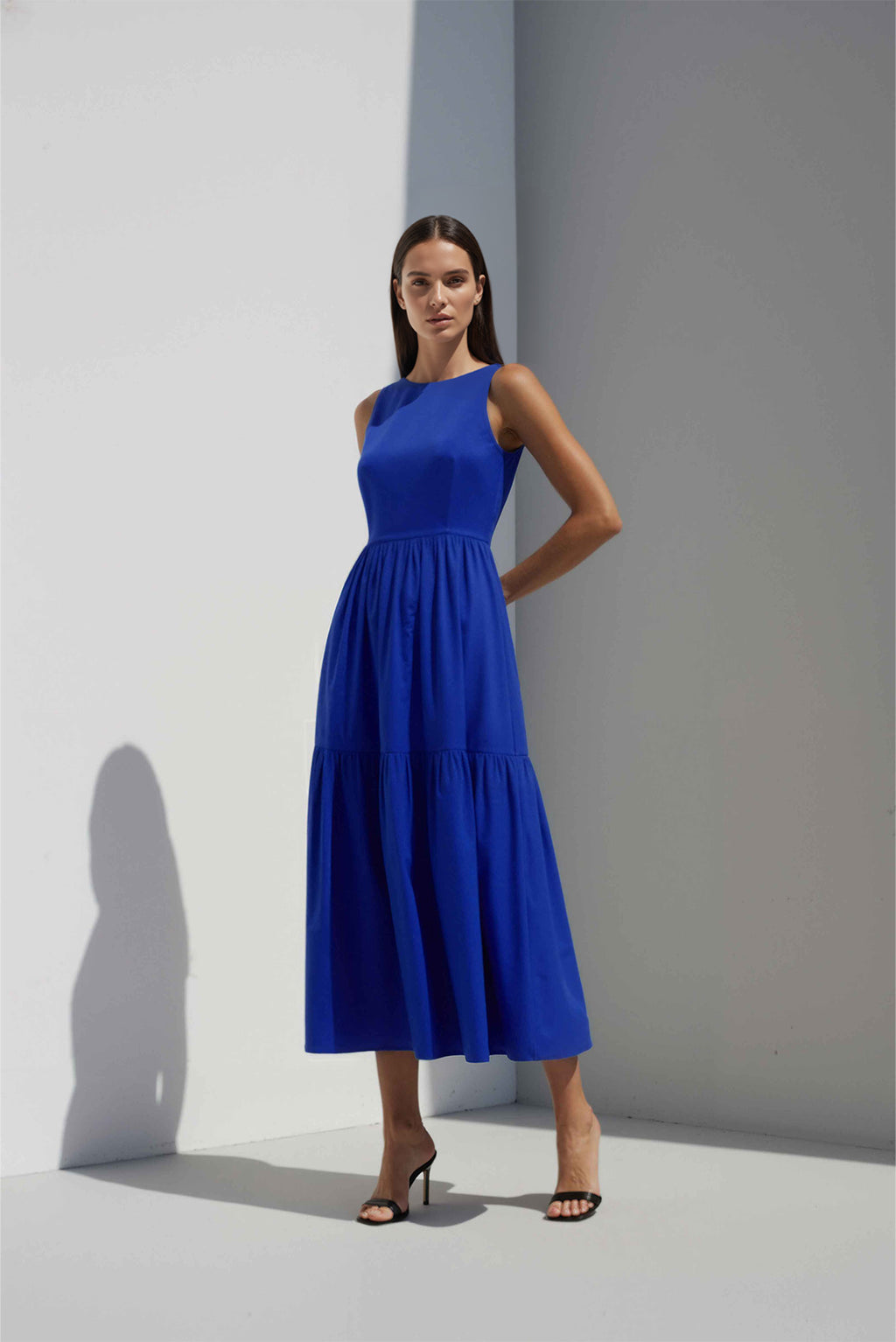 Anasua The Forme Edit Poplin Cotton Midi Dress in Sand Grey, a structured sleeveless cotton midi dress with a tiered skirt, photographed under natural sunlight.