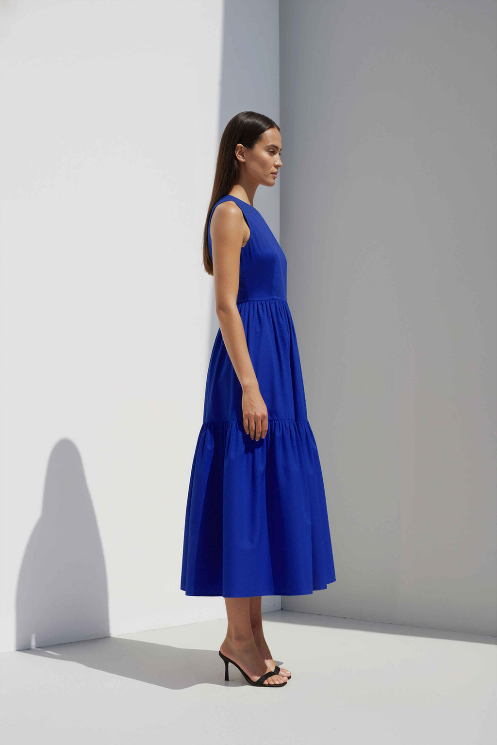 Anasua The Forme Edit Poplin Cotton Midi Dress in Sand Grey, a structured sleeveless cotton midi dress with a tiered skirt, photographed under natural sunlight.