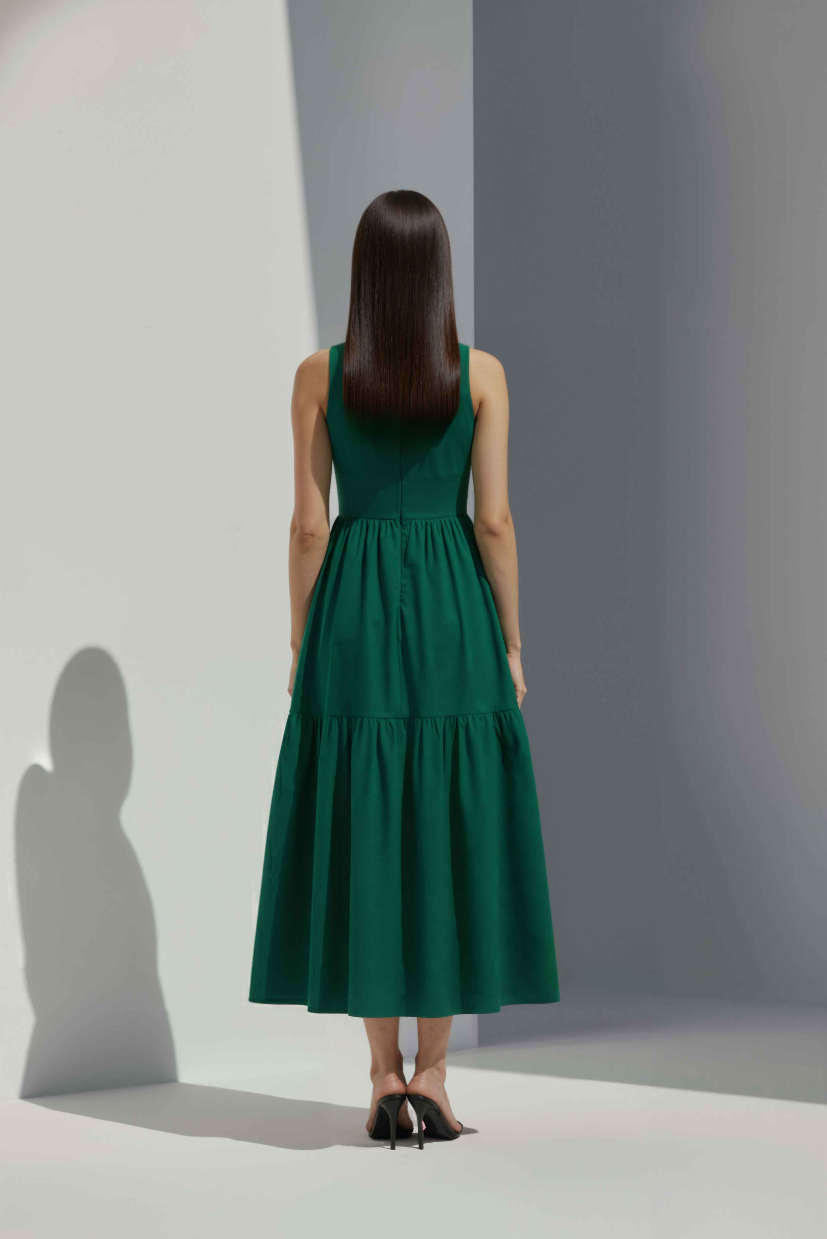 Anasua The Forme Edit Poplin Cotton Midi Dress in Verdant Green, a structured sleeveless cotton midi dress with a tiered skirt, photographed under natural sunlight.