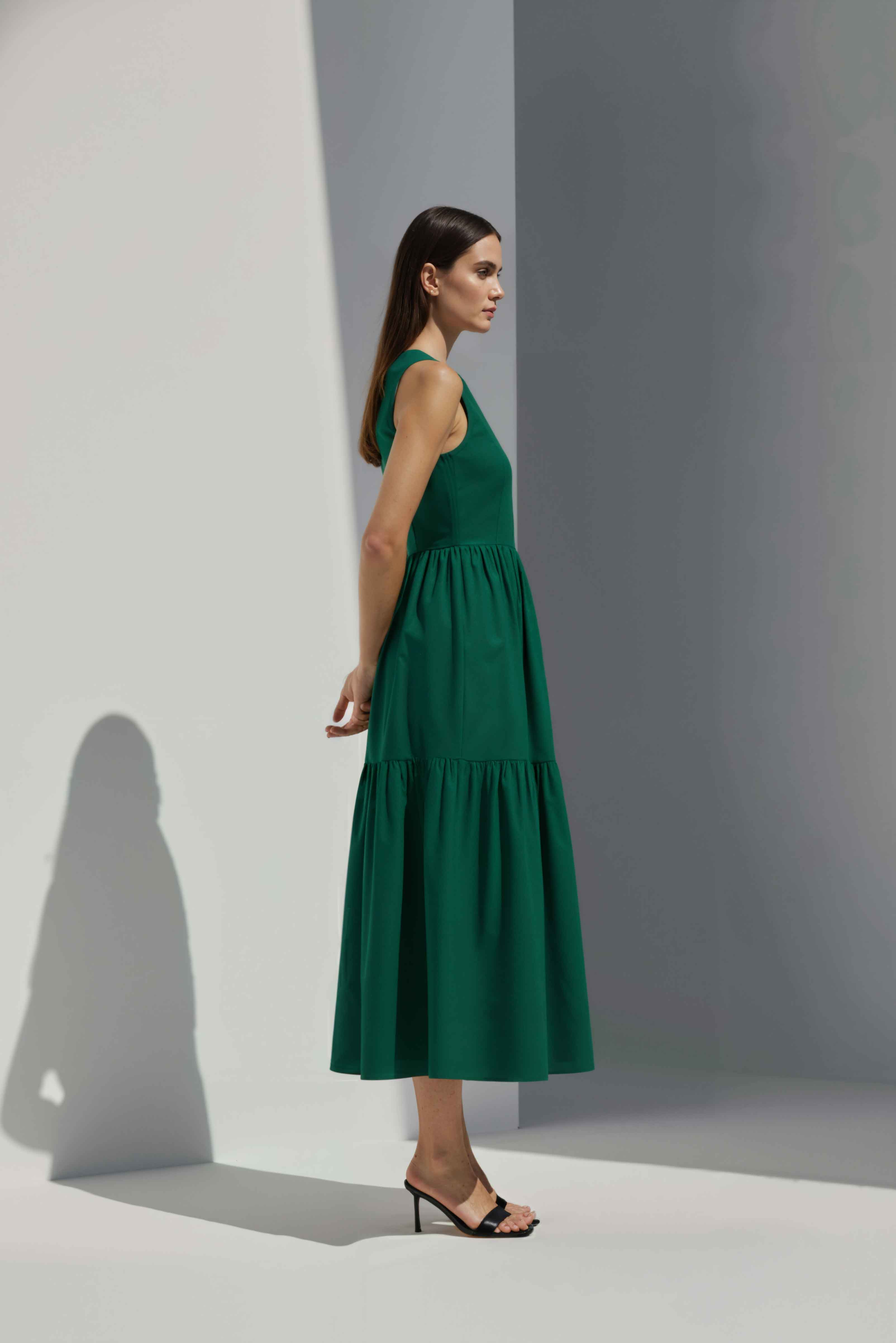 Anasua The Forme Edit Poplin Cotton Midi Dress in Verdant Green, a structured sleeveless cotton midi dress with a tiered skirt, photographed under natural sunlight.