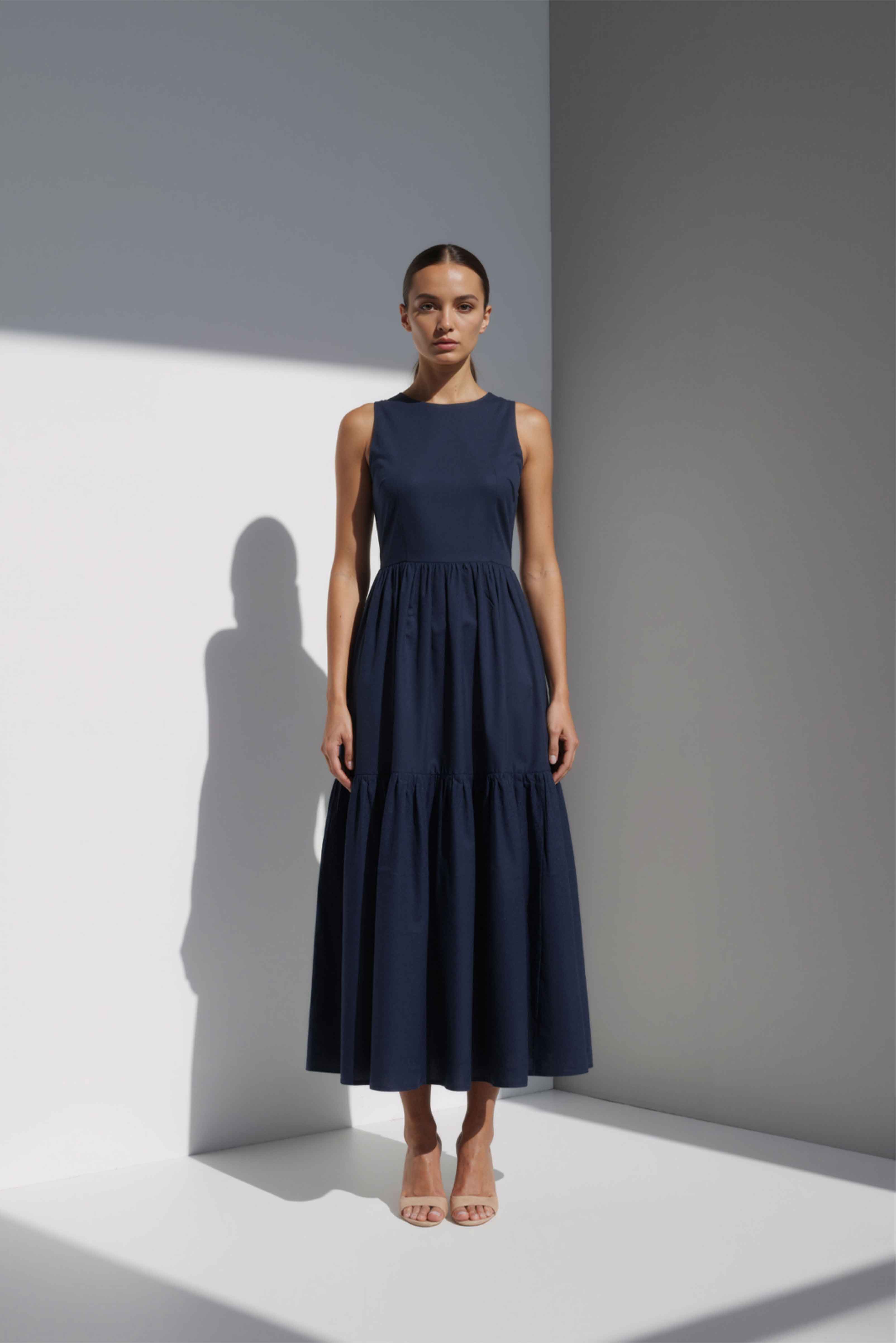 Model wearing The Forme Edit Poplin Cotton Midi Dress in Navy Blue, photographed under natural sunlight against a minimal architectural wall, highlighting the structured bodice and softly tiered skirt.