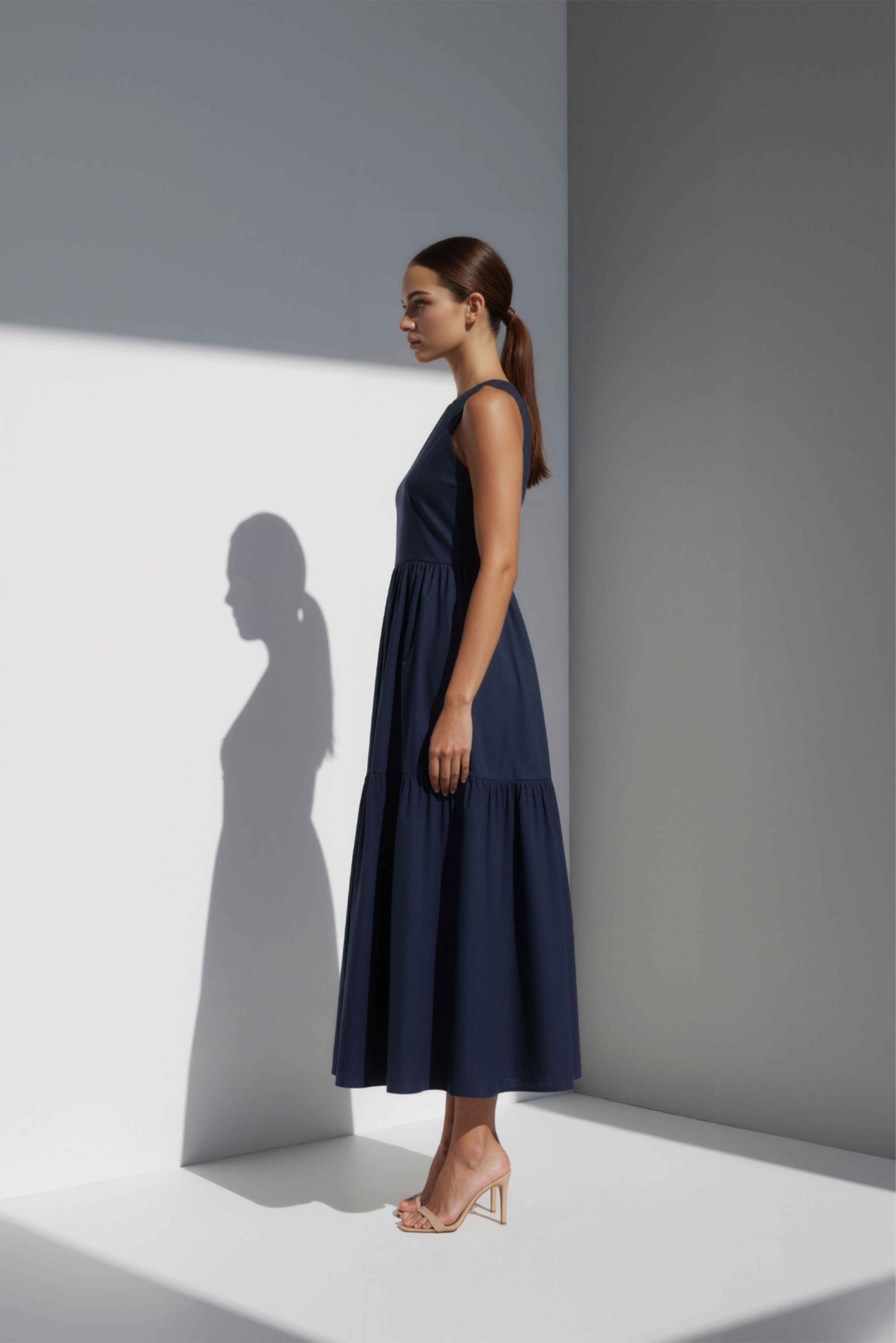 Model wearing The Forme Edit Poplin Cotton Midi Dress in Navy Blue, photographed under natural sunlight against a minimal architectural wall, highlighting the structured bodice and softly tiered skirt.