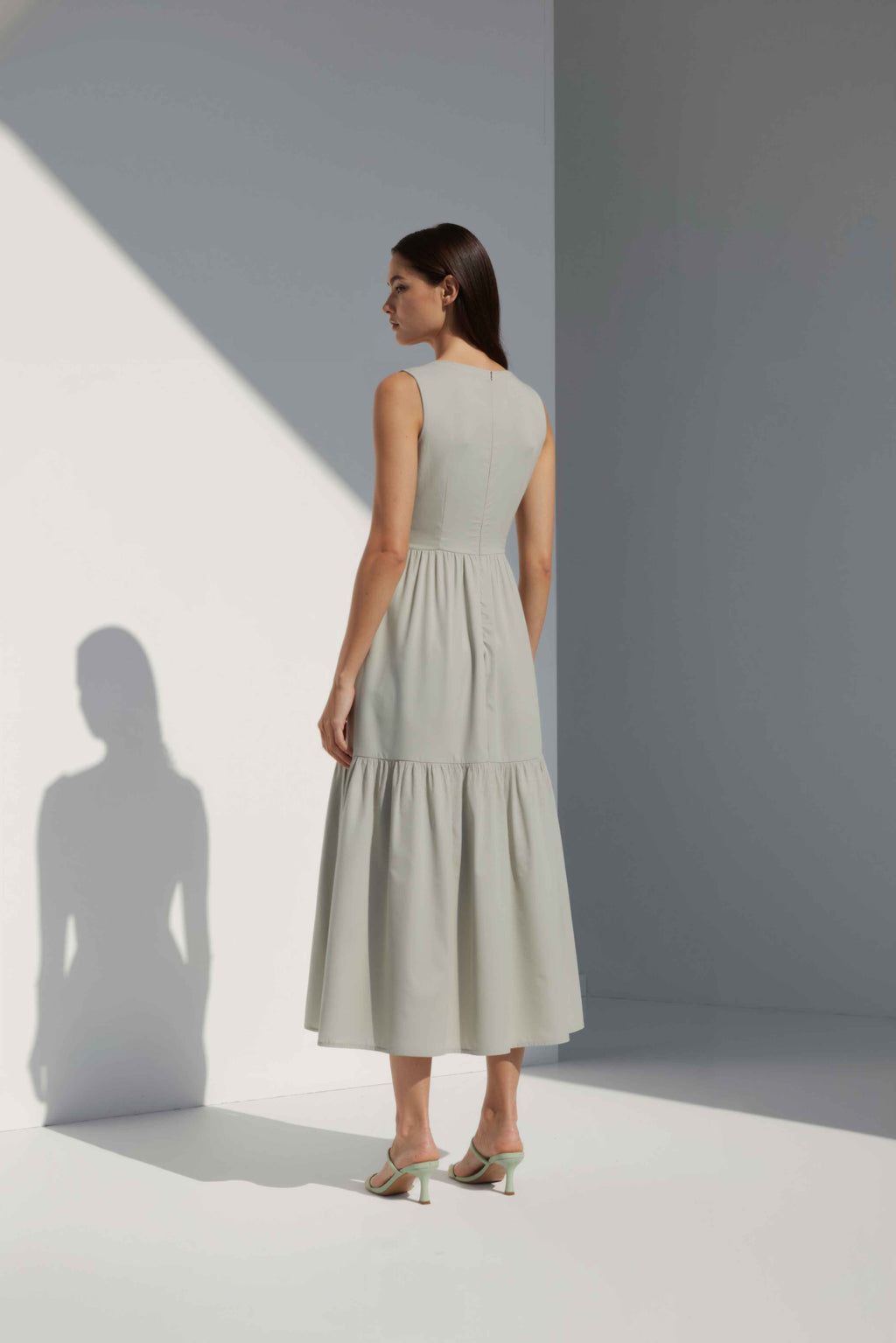 Anasua The Forme Edit Poplin Cotton Midi Dress in Sand Grey, a structured sleeveless cotton midi dress with a tiered skirt, photographed under natural sunlight.