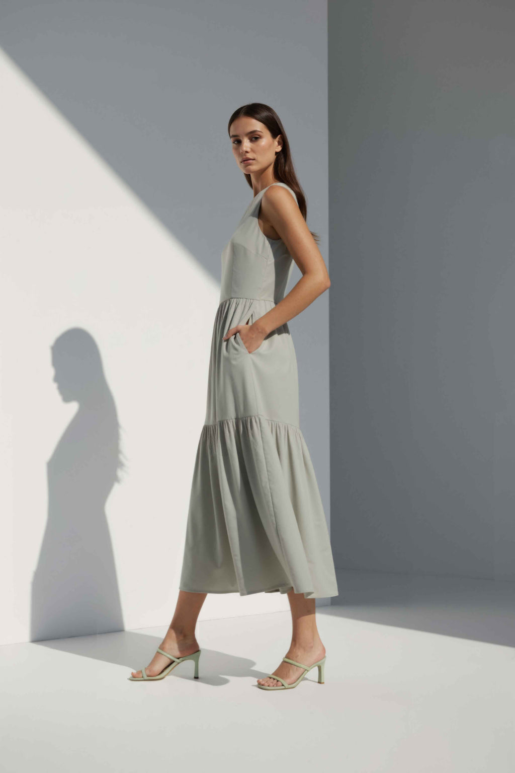 Anasua The Forme Edit Poplin Cotton Midi Dress in Sand Grey, a structured sleeveless cotton midi dress with a tiered skirt, photographed under natural sunlight.