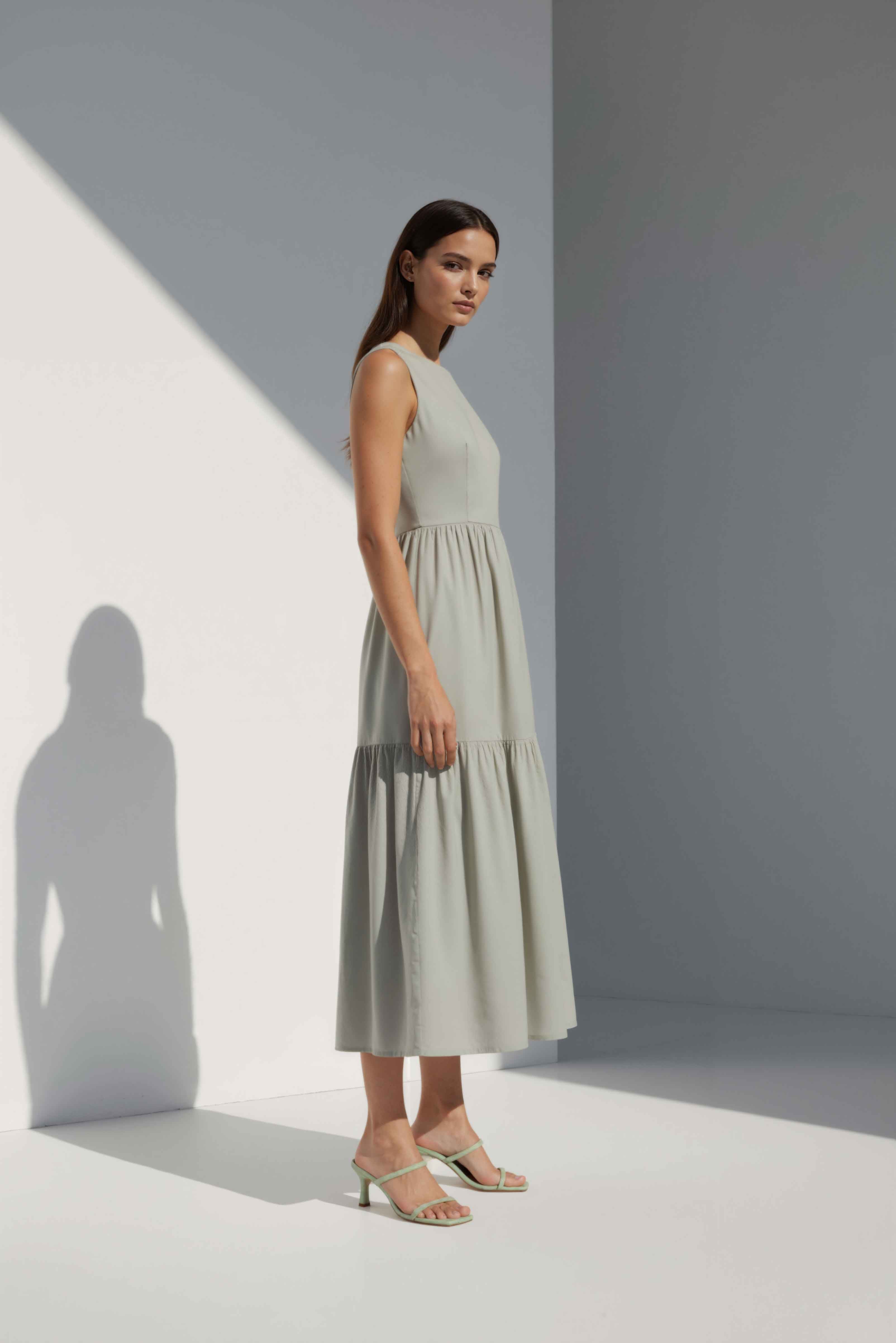 Anasua The Forme Edit Poplin Cotton Midi Dress in Sand Grey, a structured sleeveless cotton midi dress with a tiered skirt, photographed under natural sunlight.