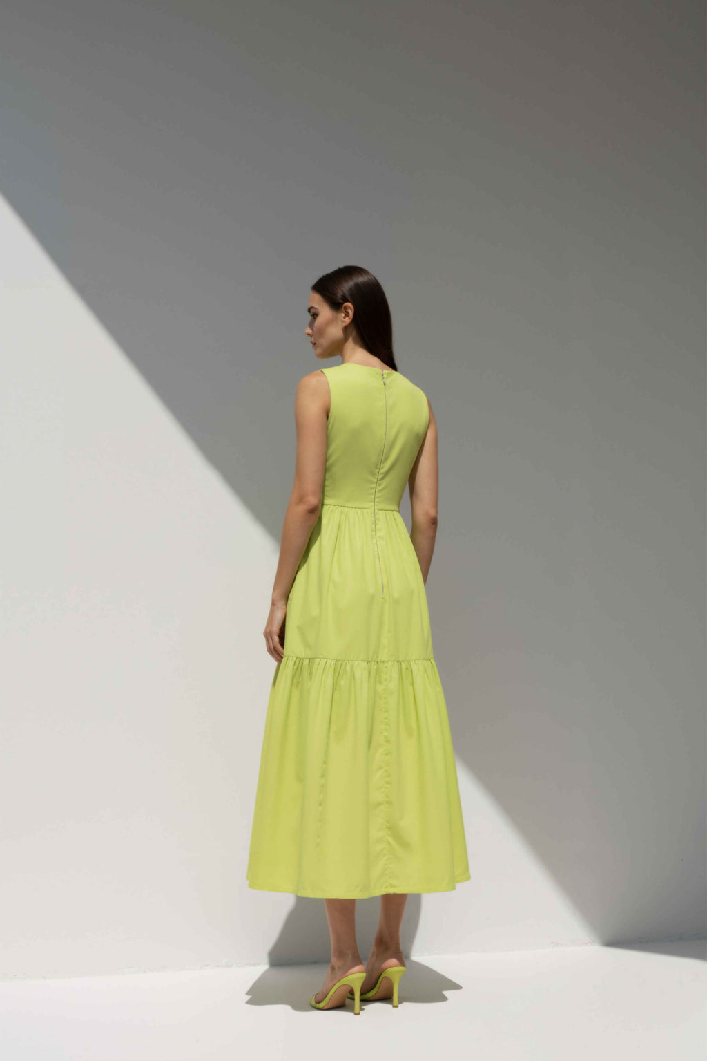 Model wearing The Forme Edit Poplin Cotton Midi Dress in Yellow, photographed under natural sunlight against a minimal architectural wall, highlighting the structured bodice and softly tiered skirt.