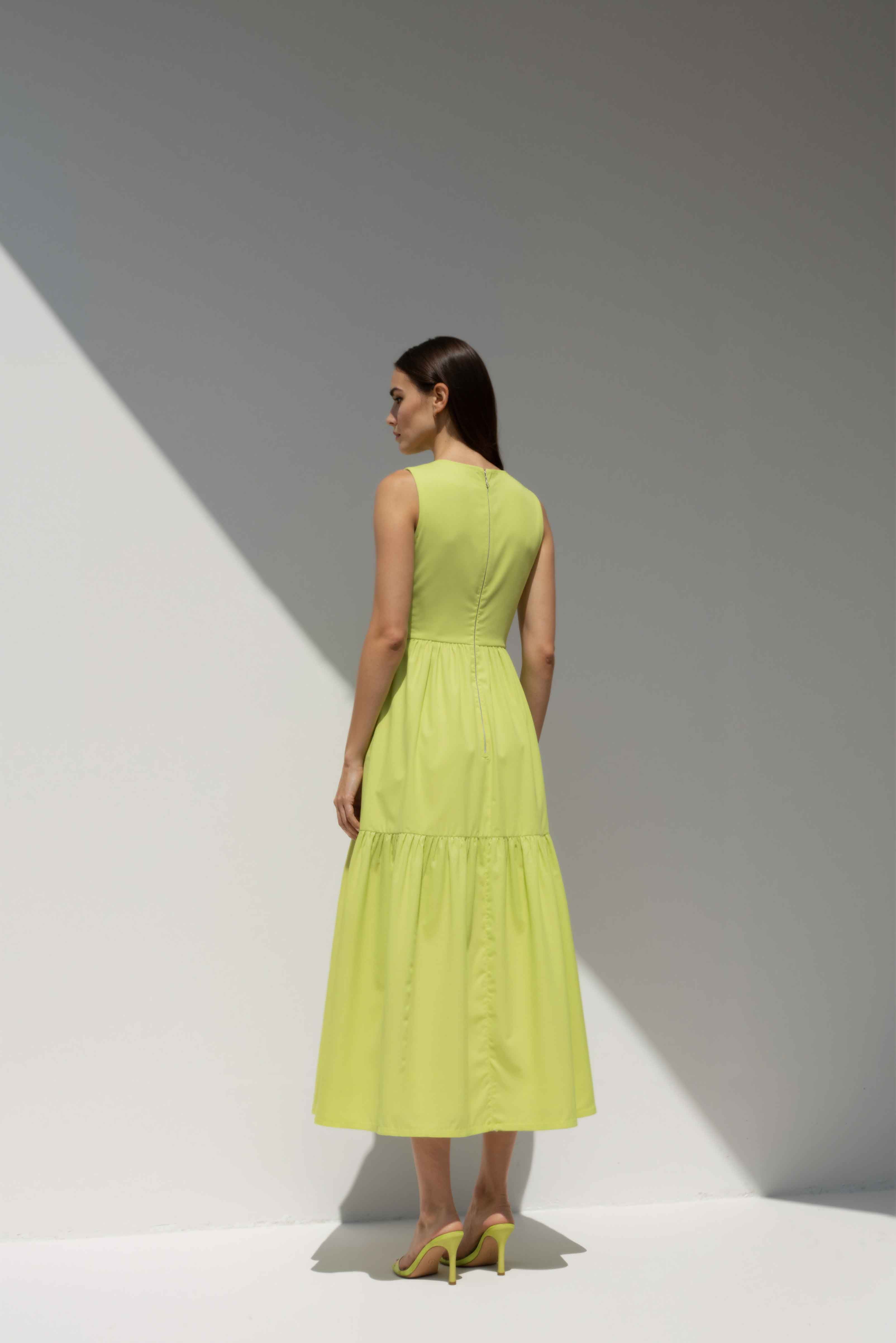 Model wearing The Forme Edit Poplin Cotton Midi Dress in Yellow, photographed under natural sunlight against a minimal architectural wall, highlighting the structured bodice and softly tiered skirt.