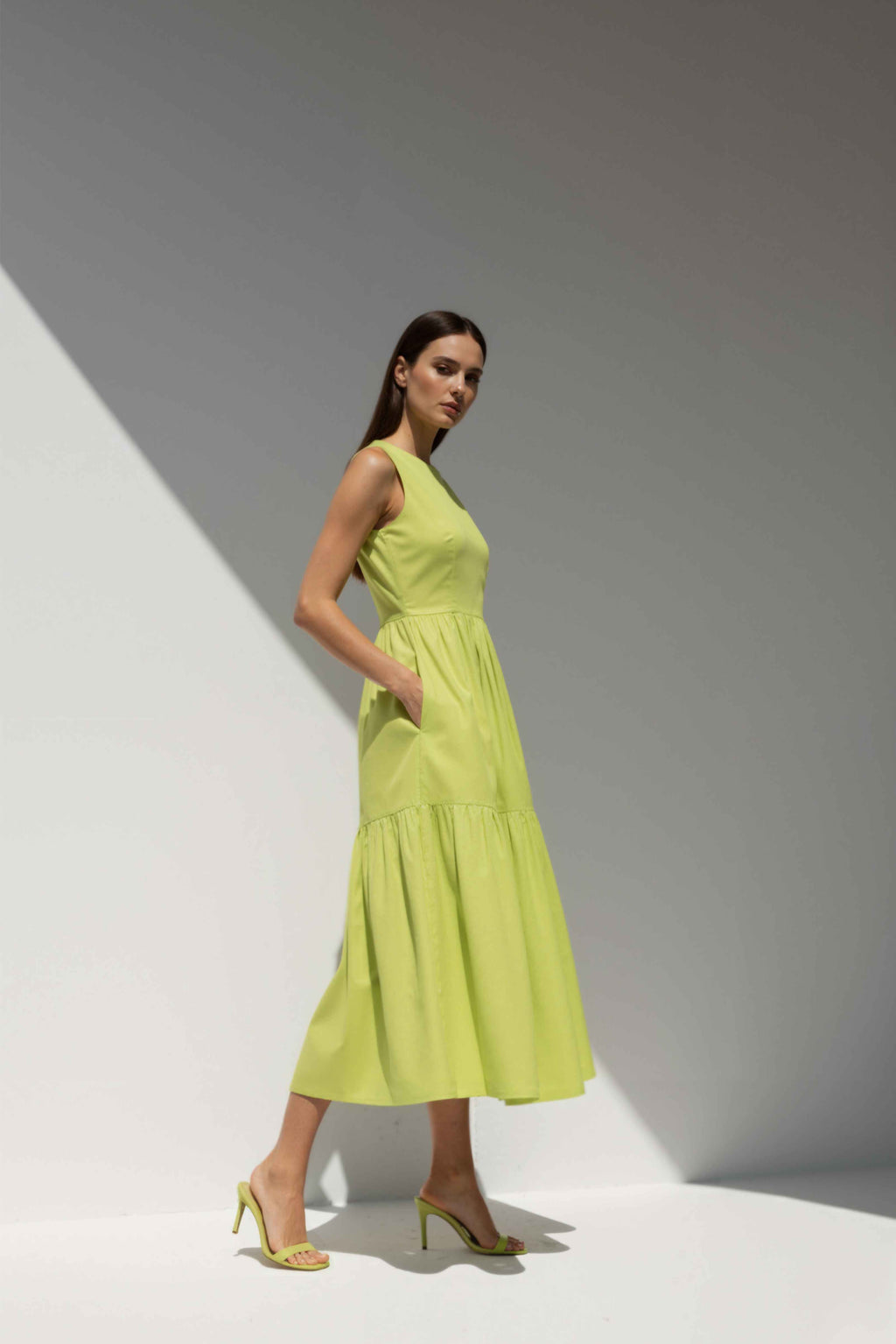 Model wearing The Forme Edit Poplin Cotton Midi Dress in Yellow, photographed under natural sunlight against a minimal architectural wall, highlighting the structured bodice and softly tiered skirt.