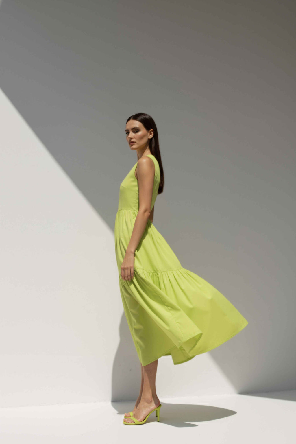 Model wearing The Forme Edit Poplin Cotton Midi Dress in Yellow, photographed under natural sunlight against a minimal architectural wall, highlighting the structured bodice and softly tiered skirt.