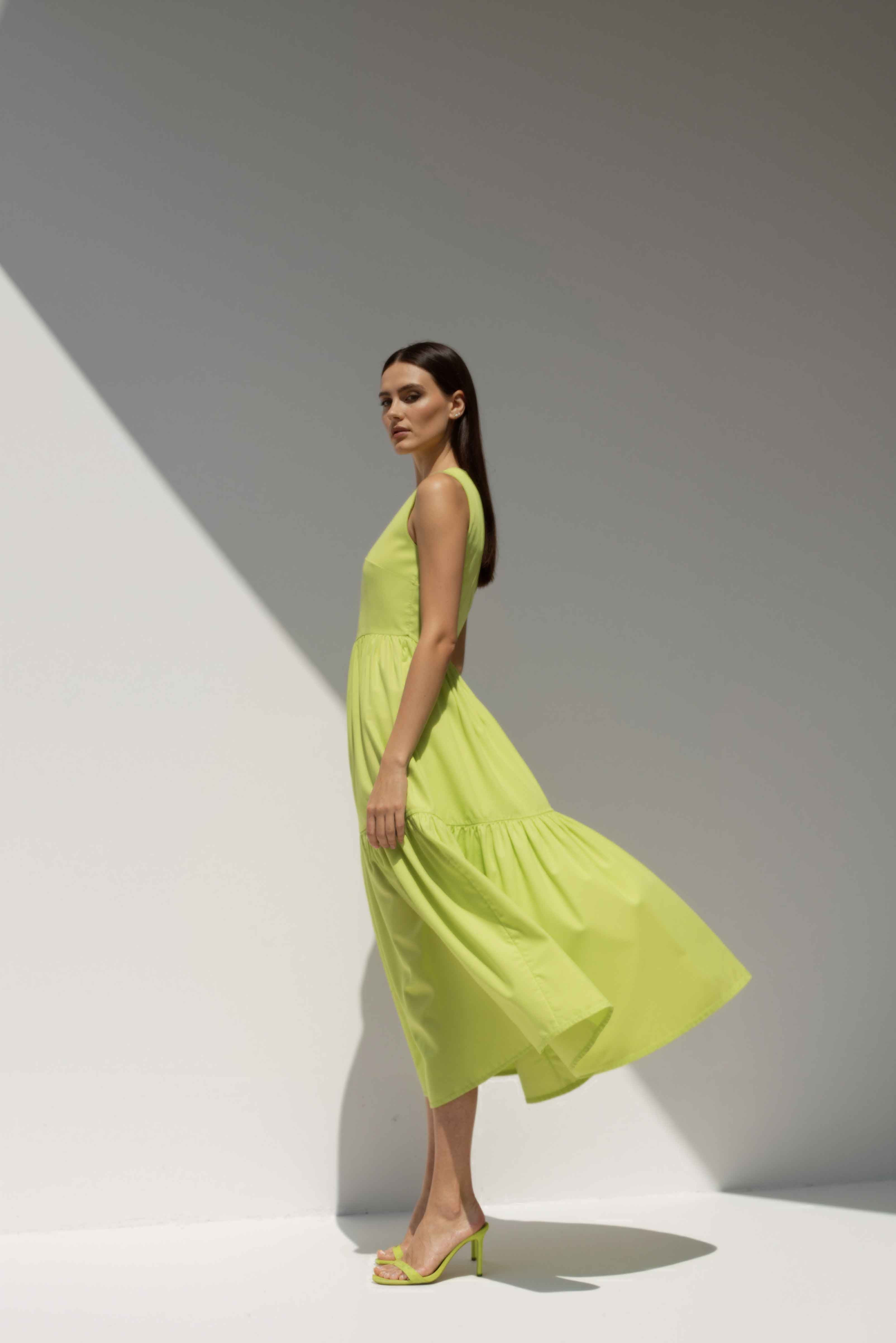 Model wearing The Forme Edit Poplin Cotton Midi Dress in Yellow, photographed under natural sunlight against a minimal architectural wall, highlighting the structured bodice and softly tiered skirt.